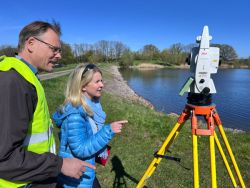 Vermessungsingenieur Fred Dummer zeigt Manuela Heise, ILB-Bereichsleiterin Infrastruktur, wie der Deich vermessen wird, um seine Standsicherheit überprüfen zu können. - Foto: LK Prignitz